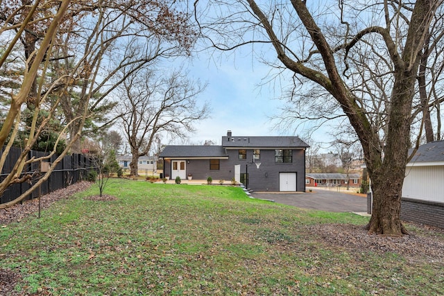 rear view of property featuring fence, a yard, a chimney, aphalt driveway, and brick siding