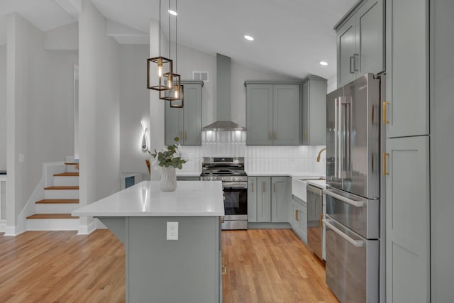 kitchen with gray cabinetry, decorative backsplash, light countertops, appliances with stainless steel finishes, and wall chimney range hood