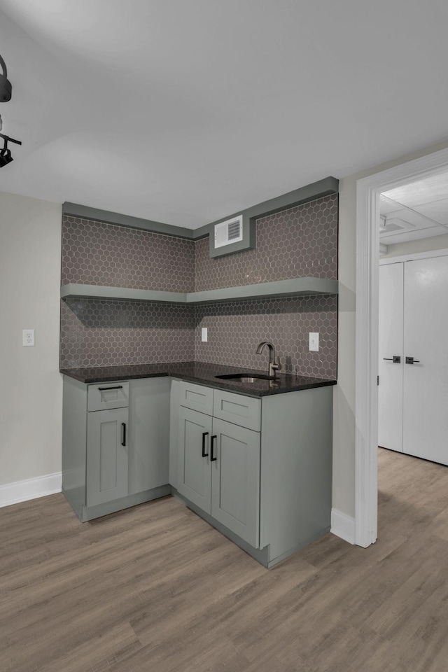 kitchen with a sink, open shelves, light wood-style flooring, and decorative backsplash