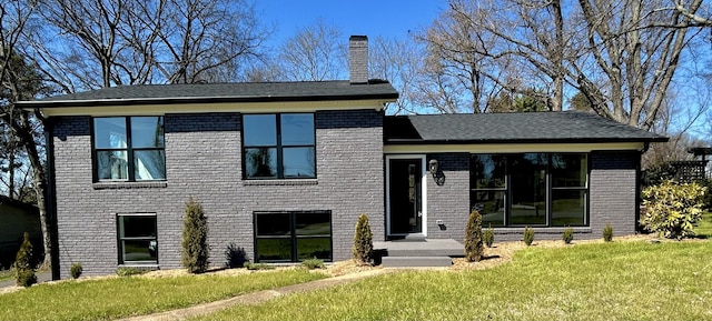 view of front of house with brick siding, a chimney, and a front yard