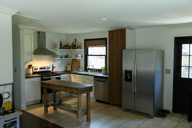 kitchen with wall chimney range hood, sink, ornamental molding, white cabinetry, and stainless steel appliances