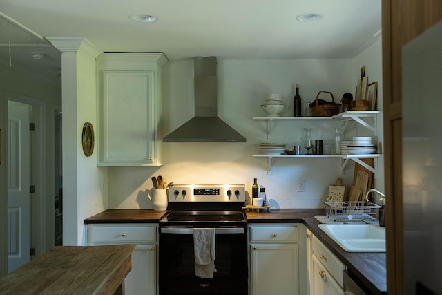 kitchen with stainless steel range with electric stovetop, wall chimney exhaust hood, wood counters, and white cabinetry