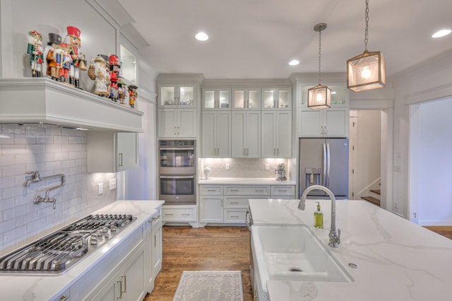 kitchen featuring pendant lighting, sink, hardwood / wood-style flooring, appliances with stainless steel finishes, and light stone counters