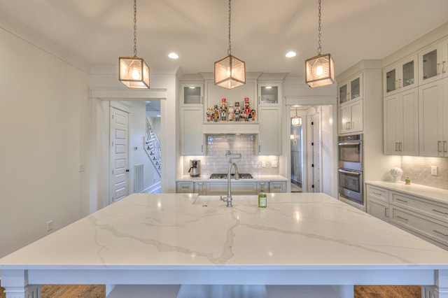 kitchen featuring tasteful backsplash, light stone counters, stainless steel appliances, a spacious island, and pendant lighting