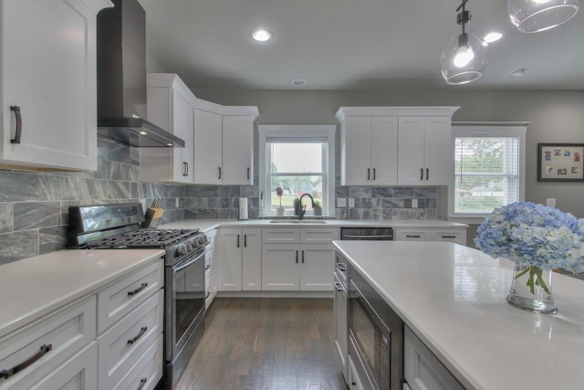 kitchen with stainless steel range with gas stovetop, white cabinetry, a healthy amount of sunlight, and wall chimney range hood