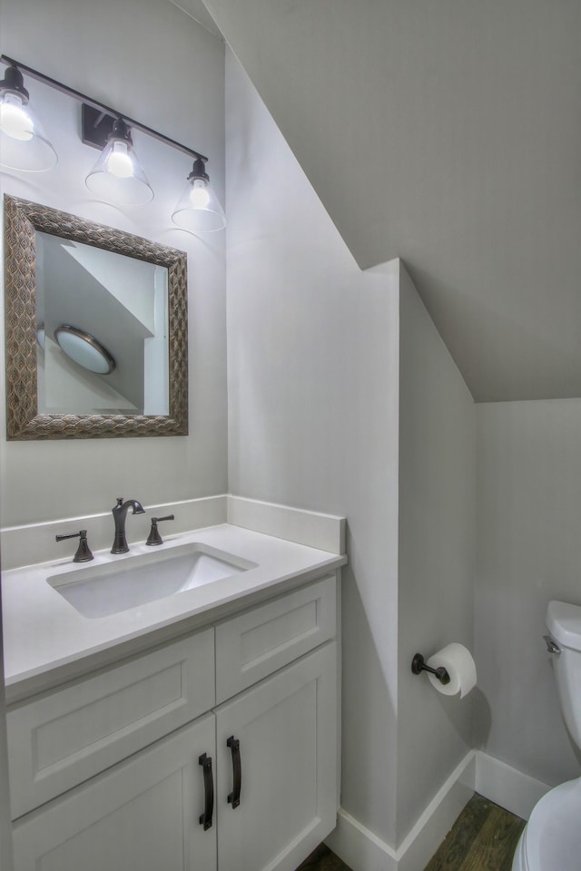 bathroom featuring vanity, toilet, wood-type flooring, and vaulted ceiling