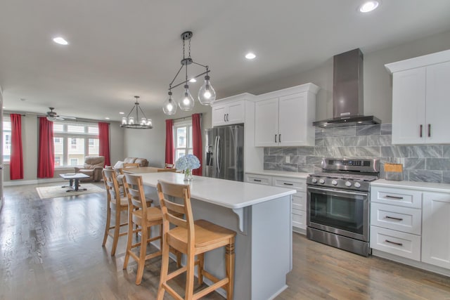 kitchen with hardwood / wood-style flooring, white cabinetry, wall chimney range hood, and appliances with stainless steel finishes