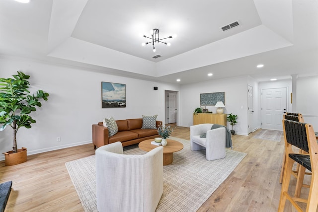 living room featuring a chandelier, light hardwood / wood-style floors, and a raised ceiling