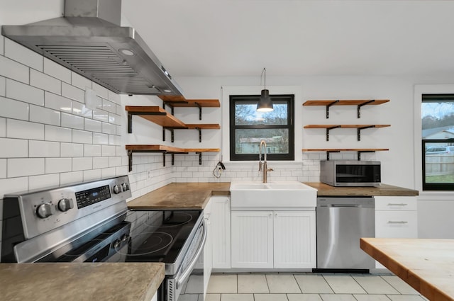 kitchen featuring pendant lighting, wall chimney range hood, sink, white cabinetry, and stainless steel appliances