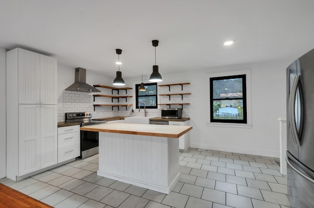 kitchen with pendant lighting, white cabinets, wall chimney range hood, butcher block counters, and stainless steel appliances