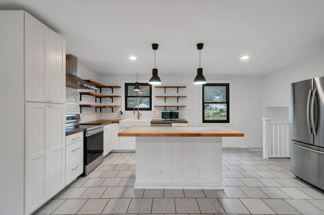 kitchen with a center island, butcher block counters, wall chimney range hood, appliances with stainless steel finishes, and white cabinetry