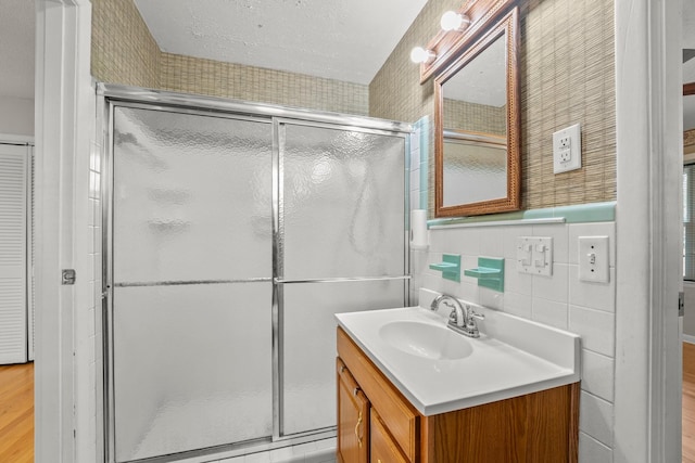 bathroom with hardwood / wood-style flooring, vanity, a shower with shower door, and tile walls