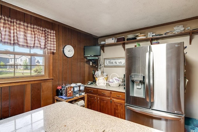 kitchen featuring stainless steel fridge, a textured ceiling, ornamental molding, and wood walls