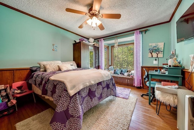 bedroom featuring ornamental molding, a textured ceiling, ceiling fan, hardwood / wood-style flooring, and wood walls