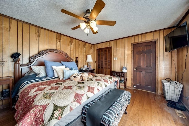 bedroom with ceiling fan, wood walls, a textured ceiling, a closet, and hardwood / wood-style flooring