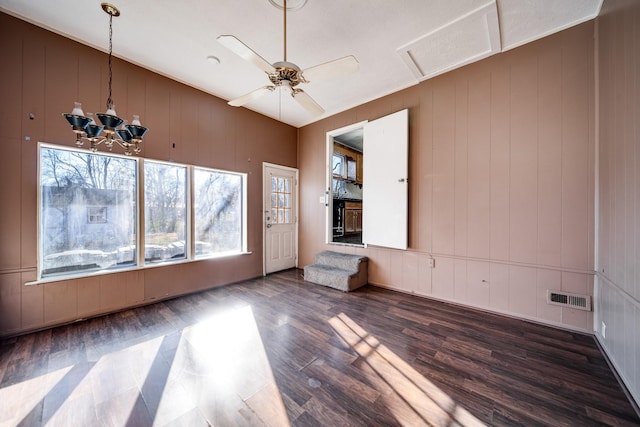 unfurnished room with dark hardwood / wood-style floors, wood walls, and ceiling fan with notable chandelier