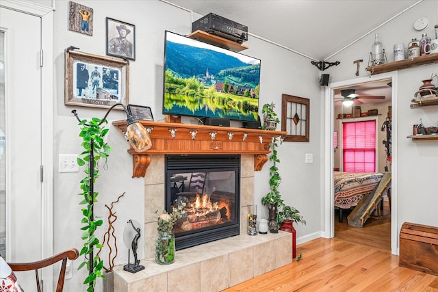 living area with ceiling fan, light wood-type flooring, and a tile fireplace