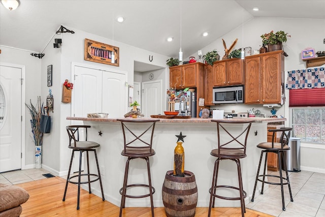 kitchen with sink, a breakfast bar, lofted ceiling, and light hardwood / wood-style flooring