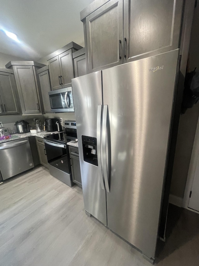 kitchen featuring light stone countertops, light wood-type flooring, and stainless steel appliances