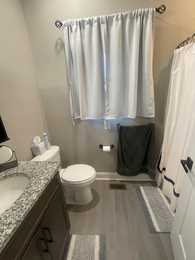 bathroom with hardwood / wood-style floors, vanity, toilet, and walk in shower