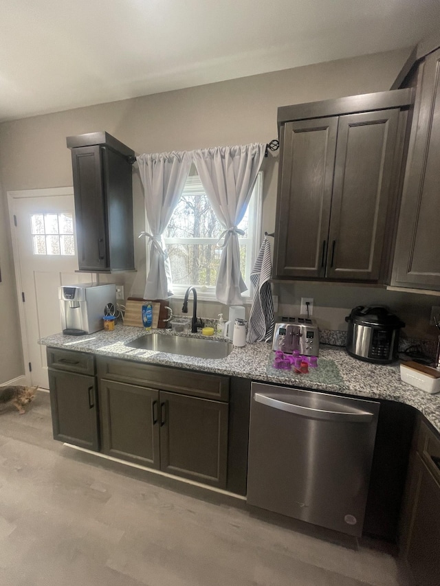 kitchen with dark brown cabinetry, light stone counters, stainless steel dishwasher, and sink