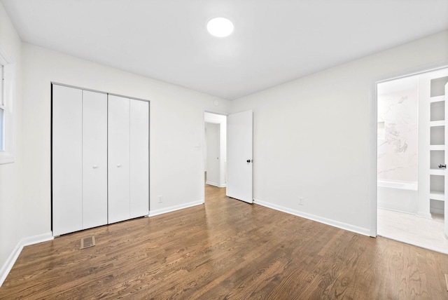 unfurnished bedroom featuring hardwood / wood-style floors, connected bathroom, and a closet