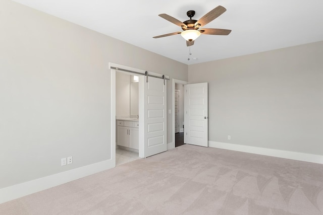 unfurnished bedroom featuring connected bathroom, a barn door, ceiling fan, and light carpet