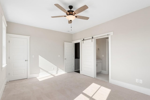 unfurnished bedroom with a barn door, ensuite bathroom, ceiling fan, and light colored carpet