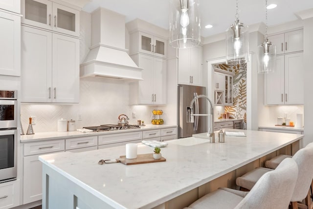 kitchen with pendant lighting, a center island with sink, white cabinets, custom range hood, and stainless steel appliances