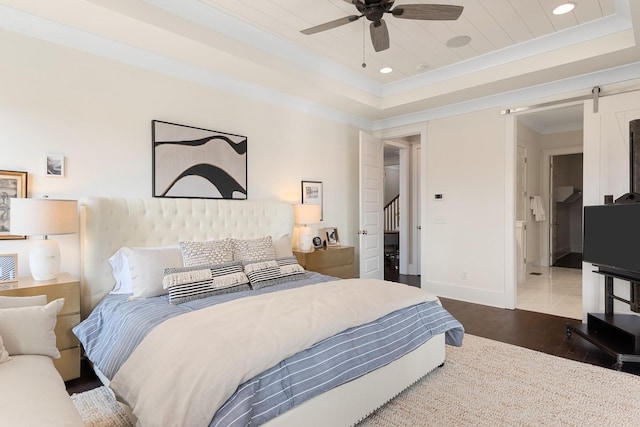 bedroom with hardwood / wood-style floors, ceiling fan, a barn door, and a tray ceiling