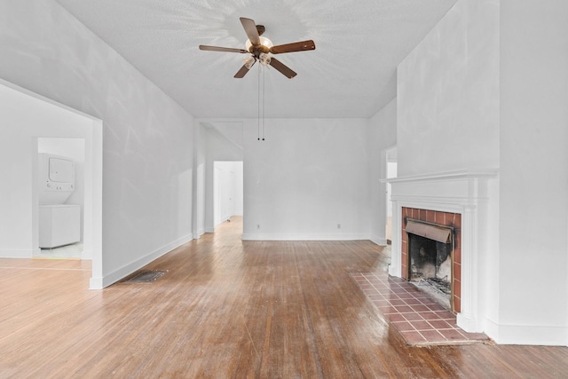 unfurnished living room with hardwood / wood-style flooring, ceiling fan, a textured ceiling, and a tiled fireplace