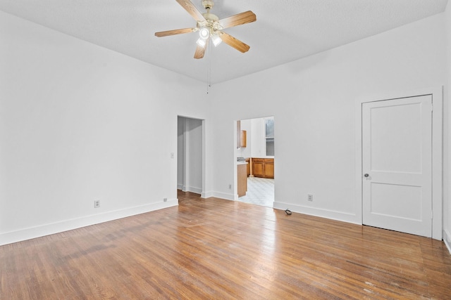 empty room featuring a high ceiling, light wood-type flooring, a textured ceiling, and ceiling fan