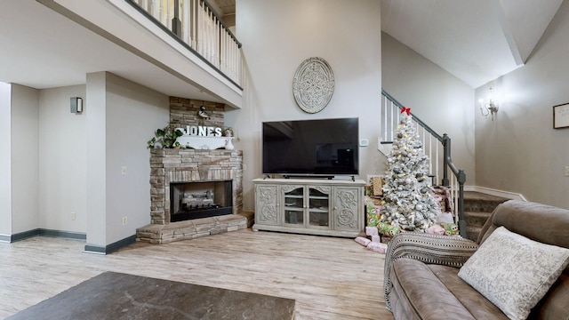 living room with a stone fireplace, a high ceiling, and hardwood / wood-style flooring