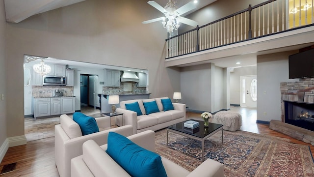 living room with ceiling fan, light hardwood / wood-style floors, a stone fireplace, and a high ceiling