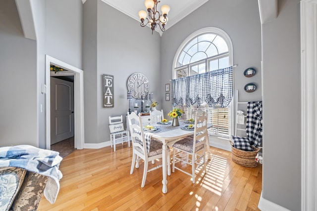 dining space featuring a towering ceiling, hardwood / wood-style flooring, an inviting chandelier, and ornamental molding