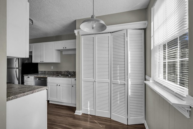 kitchen with stainless steel appliances, a sink, dark wood-type flooring, white cabinets, and a textured ceiling