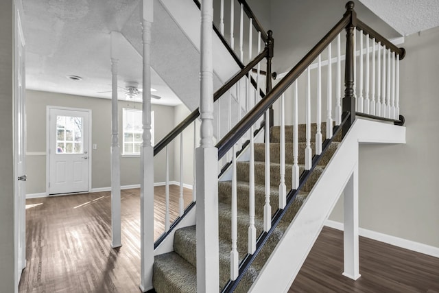 stairs featuring ceiling fan, wood finished floors, baseboards, and a textured ceiling