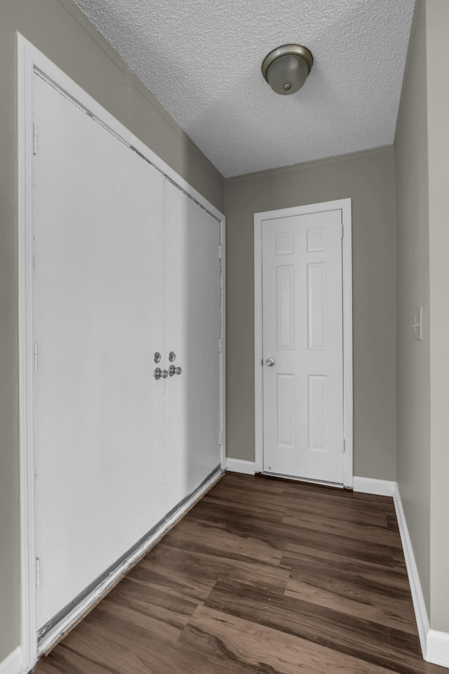 unfurnished bedroom featuring a closet, a textured ceiling, dark wood-type flooring, and baseboards