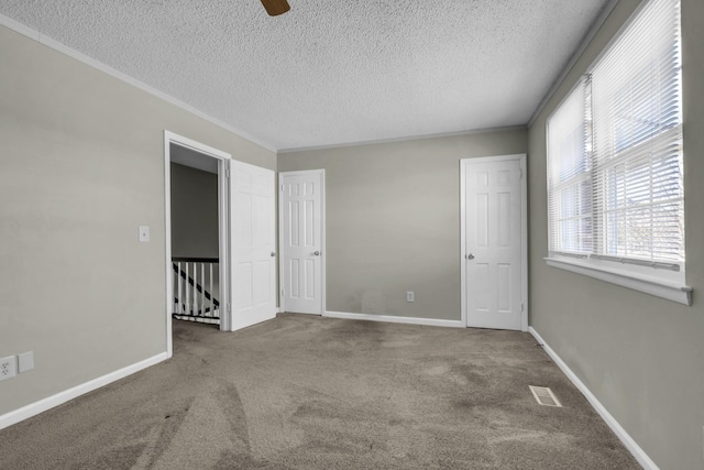 carpeted spare room with visible vents, baseboards, a textured ceiling, and crown molding