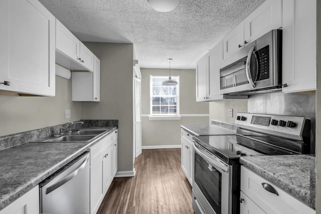 kitchen with baseboards, a sink, dark wood-type flooring, appliances with stainless steel finishes, and white cabinetry