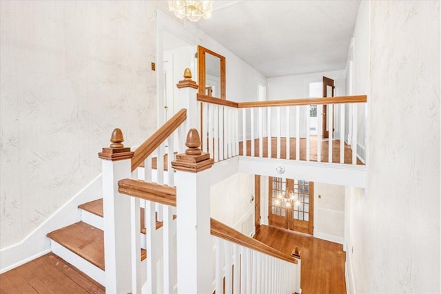 stairway with french doors, hardwood / wood-style flooring, and an inviting chandelier