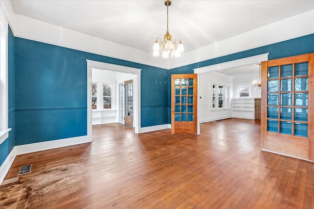 unfurnished room with french doors, an inviting chandelier, a textured ceiling, and hardwood / wood-style flooring