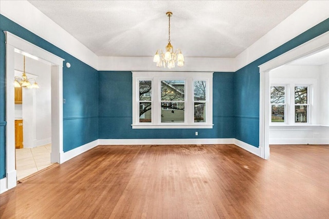 unfurnished dining area featuring hardwood / wood-style floors, a textured ceiling, an inviting chandelier, and a healthy amount of sunlight