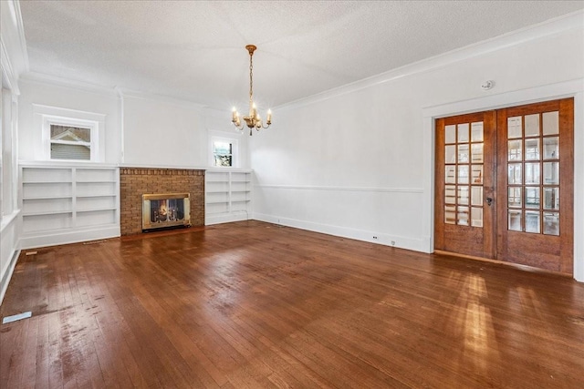 unfurnished living room with french doors, a brick fireplace, a textured ceiling, dark hardwood / wood-style flooring, and a chandelier