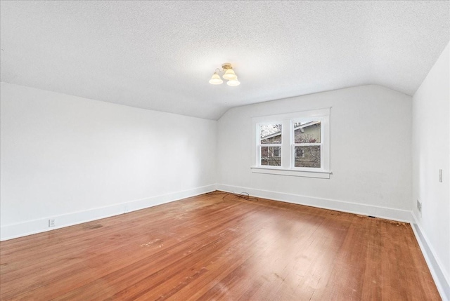 additional living space featuring wood-type flooring, a textured ceiling, and vaulted ceiling