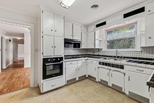 kitchen featuring tile counters, sink, tasteful backsplash, black oven, and white cabinets