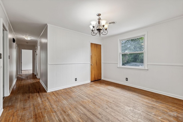 empty room featuring crown molding, a notable chandelier, and hardwood / wood-style flooring