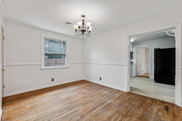 unfurnished room featuring hardwood / wood-style floors, ornamental molding, and an inviting chandelier