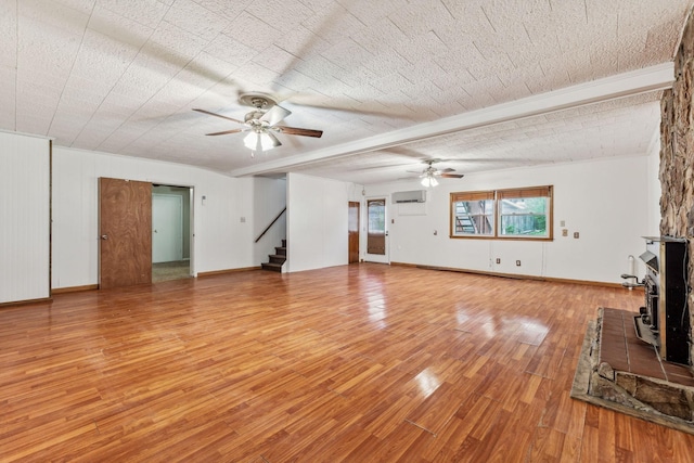 unfurnished living room with ceiling fan, beamed ceiling, an AC wall unit, hardwood / wood-style floors, and a textured ceiling