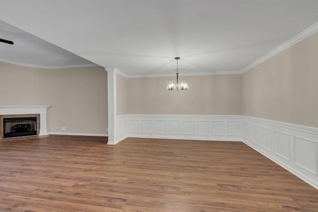 unfurnished dining area featuring a tiled fireplace, hardwood / wood-style flooring, crown molding, and an inviting chandelier